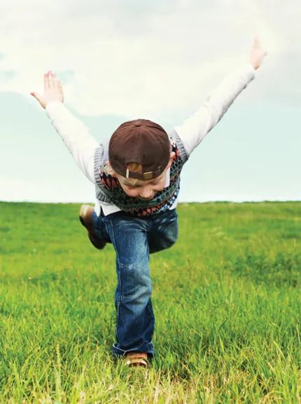 A child with arms outstretched in a green field